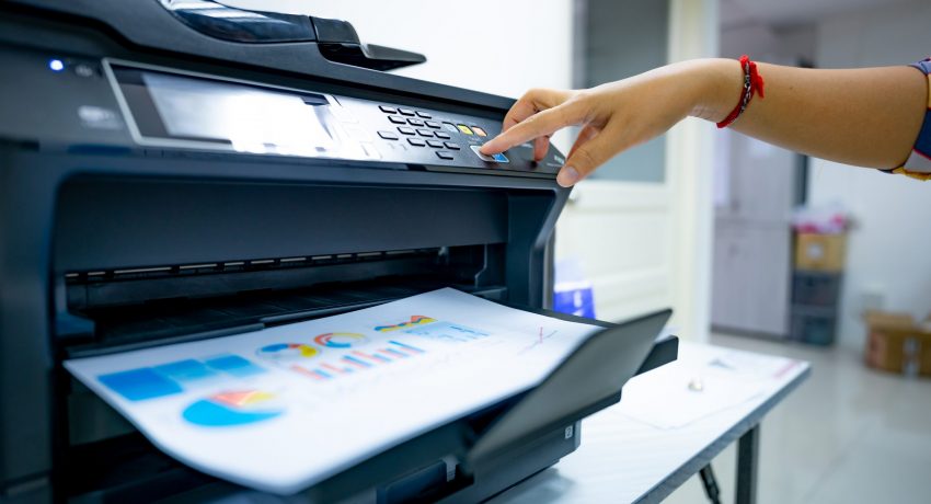 Office worker prints paper on multifunction laser printer. Copy, print, scan, and fax machine in office. Document and paper work. Print technology. Hand press on photocopy machine. Scanner equipment.