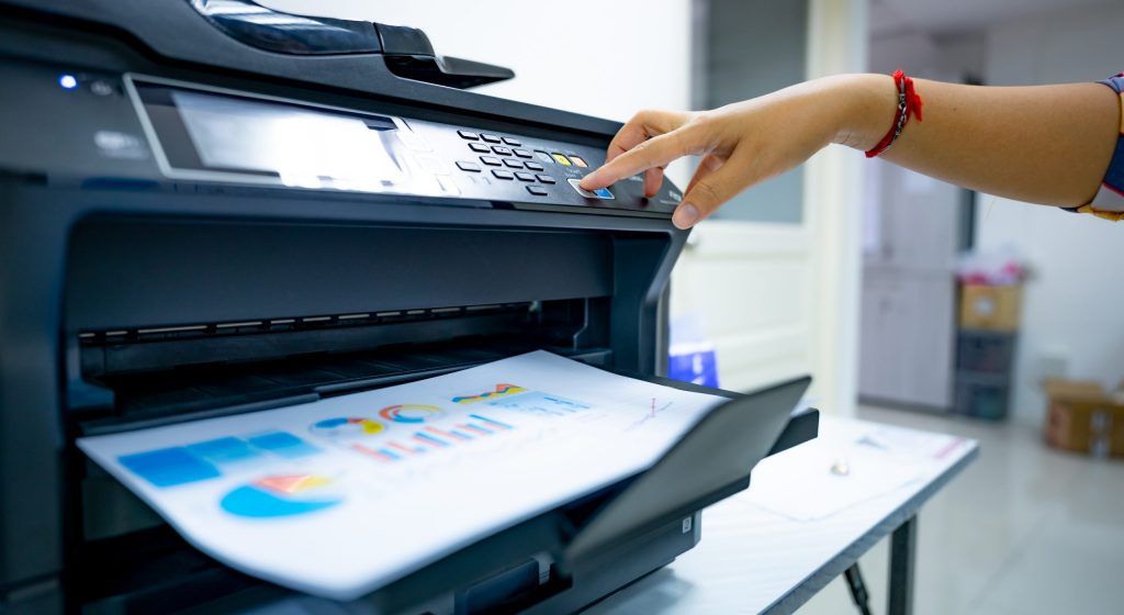 Office worker prints paper on multifunction laser printer. Copy, print, scan, and fax machine in office. Document and paper work. Print technology. Hand press on photocopy machine. Scanner equipment.